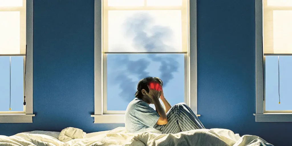 Person sitting on bed holding head with red glowing temples, indicating migraine pain.