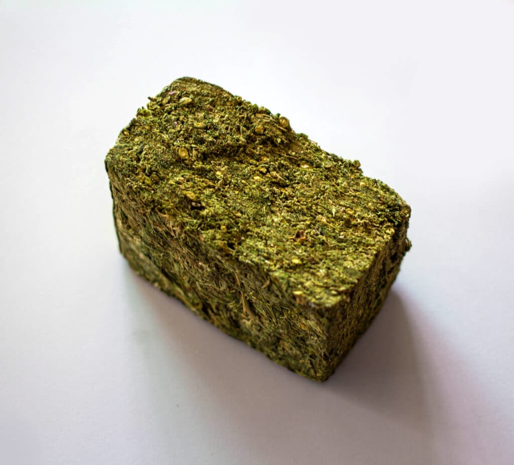 A compacted block of hashish with a bumpy, golden-green texture on a wooden surface.