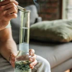 Close-up of hands lighting a water bong with cannabis in a cozy home setting.