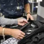 Passenger packing a vape in their carry-on bag at airport security, showing rules on can you bring a vape on a plane.