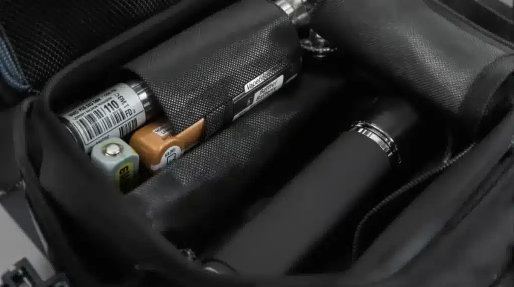 Vape batteries and devices organized in a black travel bag compartment.
