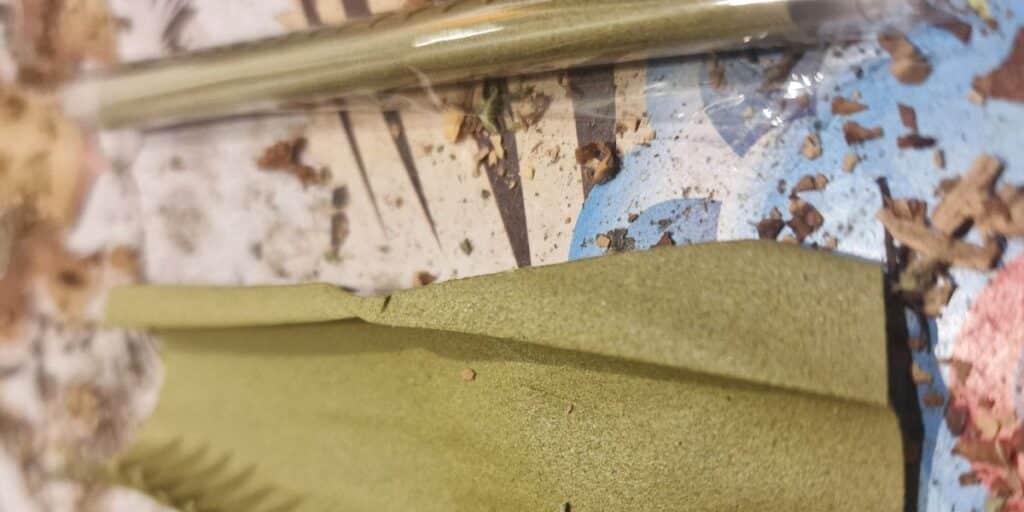 Close-up of green hemp blunt wrap and sealed blunt on a textured surface with herb pieces.