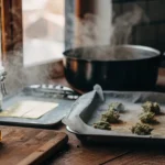 Kitchen counter with cannabis buds on a tray, butter, and a steaming pot.