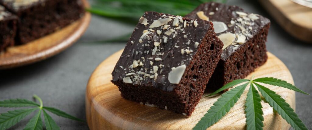 Cannabis-infused brownies placed on a wooden board with cannabis leaves