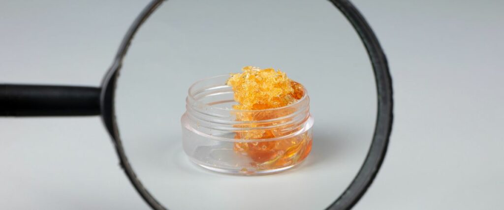 Cannabis concentrate in a small jar under a magnifying glass