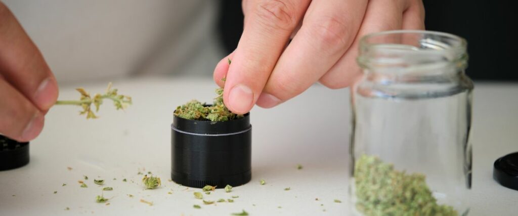 Close-up of a person using a handheld grinder to prepare cannabis.