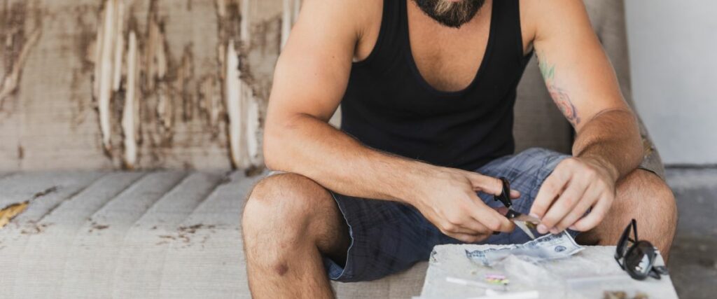 Man outdoors preparing cannabis with a handheld grinder.
