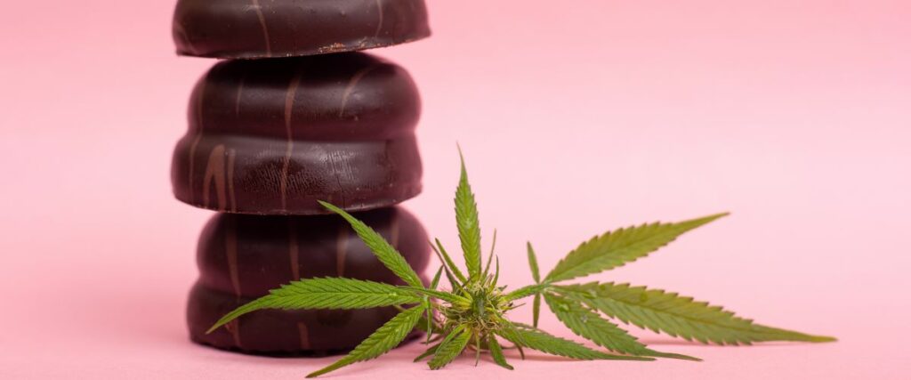 Stacked chocolate THC edibles with a cannabis leaf on a pink background.