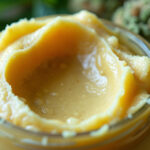 Batter THC: Close-up of a jar filled with creamy cannabis batter, showcasing its smooth texture and golden color, with cannabis buds in the background.