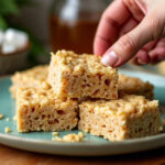 A hand picking up a piece of Cannabis Rice Krispie Treat from a plate, highlighting the discreet and tasty nature of these edibles.