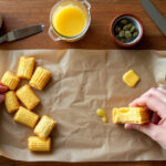 Hands preparing firecracker edibles with crackers, butter, and cannabis on a wooden table.