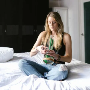 Woman sitting on bed holding a glass bong, preparing for a session.