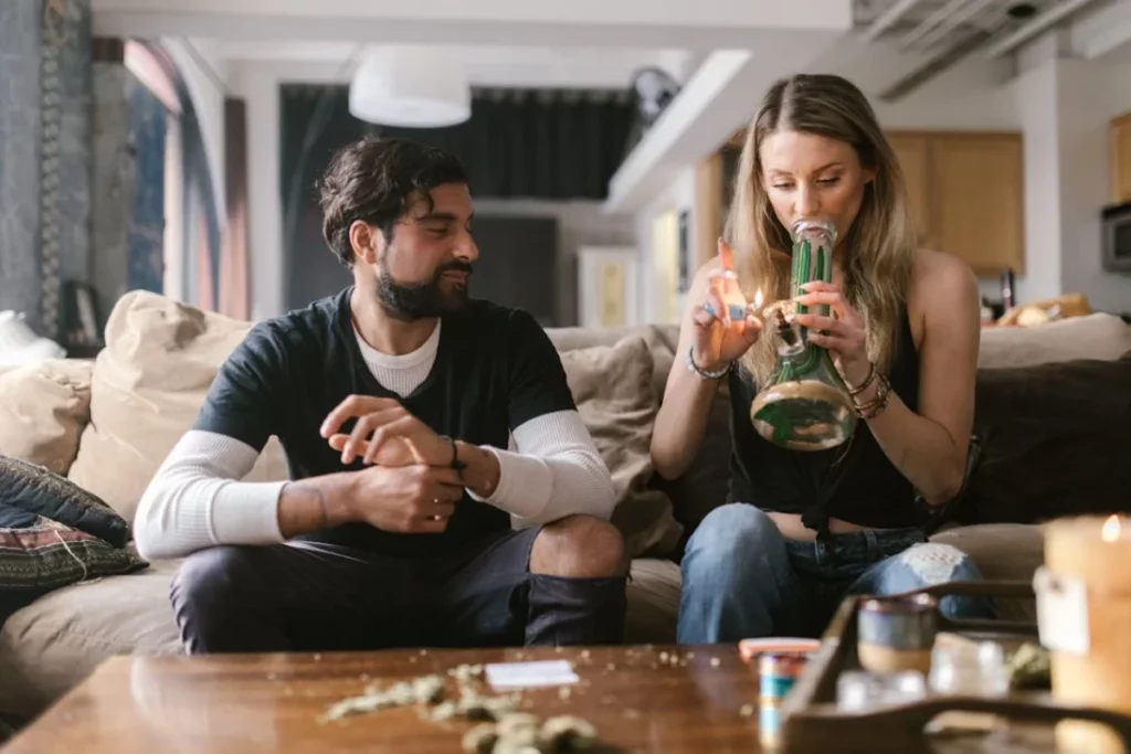 Man watching as a woman lights a bong for a smoking session on the couch.