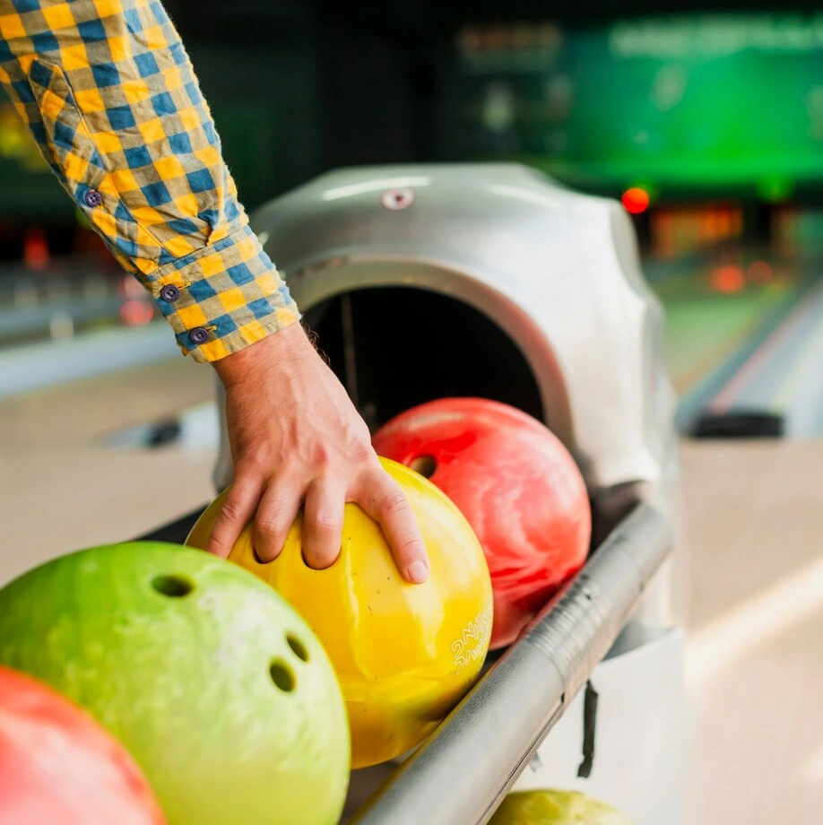 Close-up of a person selecting a bright yellow bowling ball, hinting at the casual fun atmosphere of a weed bowling event.