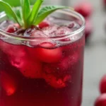 A glass of vibrant red cherry juice with ice cubes and cannabis leaves, surrounded by fresh cherries.