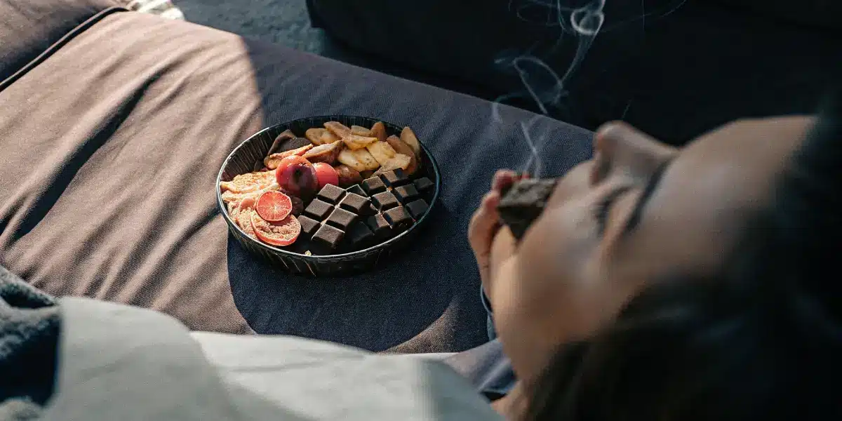 Close-up of a person's mouth, with white light trails above, near a wooden bowl of chocolate and a platter of food with red slices.