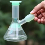 A hand holding a small, clear glass bong with green accents, ideal for a minimalist smoking experience.