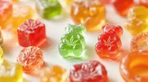 Colorful THC gummies in various shapes, including bears and cubes, with cannabis leaf icons embossed on some gummies