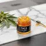 Golden THCA live rosin in a jar with cannabis leaves and a dab tool.