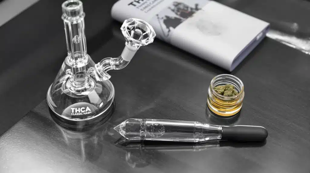 A well-organized setup with a glass dab rig, THCA classic hash in a small container, and a dab tool arranged on a sleek table. The setting emphasizes the sophistication of using THCA hash, capturing a clean and professional cannabis experience.