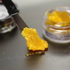 THCP solventless rosin on a dab tool beside a jar of cannabis concentrates.
