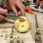 Crafting an apple pipe for smoking cannabis using a knife, with household items on a kitchen counter.