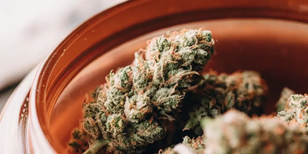 OG Glue cannabis bud with frosty trichomes stored in a glass jar, showcasing its vibrant green and orange hues.