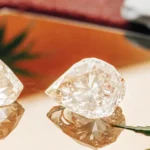 Two clear THCA crystals reflecting on a golden surface, beside a cannabis leaf.