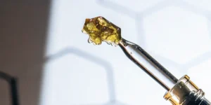 Hyper-realistic close-up of golden, crystalline THCA dabs on the tip of a glass dropper.