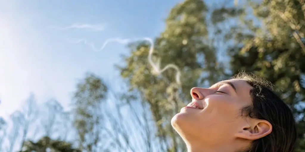 Woman with eyes closed, smiling, inhaling fresh air with wavy lines in the sky.