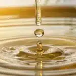 Golden drop of cbd oil splashing into water, creating gentle ripples under warm sunlight