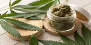 CBD Moonrock jar on wooden surface with cannabis leaves under soft natural light.