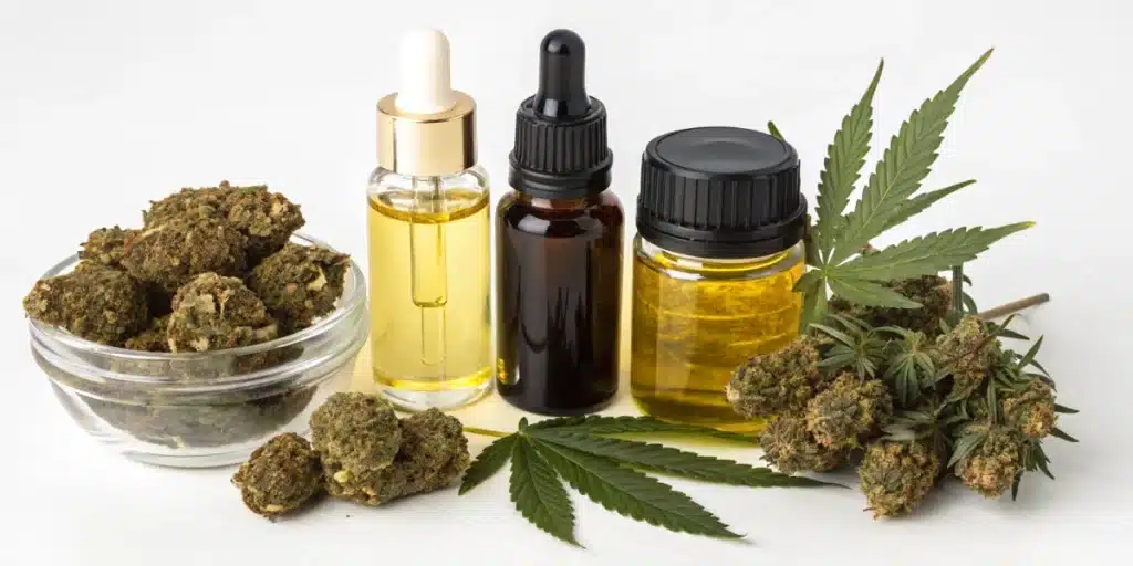 Glass bowl of cannabis buds, two dropper bottles of cannabis oil, and a cannabis leaf, against a white background.  