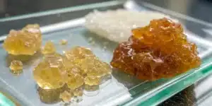 Realistic close-up of live resin and rosin samples on a glass surface, emphasizing distinct textures and colors.