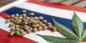 Cannabis seeds and a hemp leaf placed on a Thai flag, symbolizing legalization and cultivation.