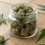 Close‑up of chunky buds from 90’s weed strains in a glass jar on a wooden surface.