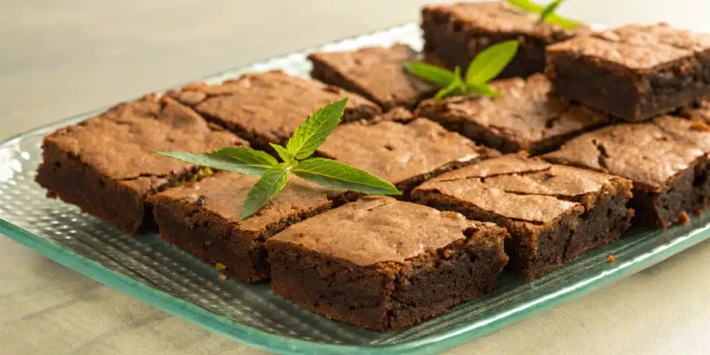 Realistic image of freshly baked weed brownies on a plate with a garnish of cannabis leaves, showcasing the final product.
