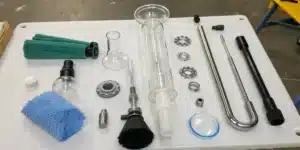 Realistic image showing how to clean a percolator bong with disassembled parts and cleaning supplies on a workbench.
