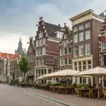 A realistic street view of Amsterdam highlighting distinctive local architecture and outdoor seating, with gentle cues about Amsterdam’s weed regulations.
