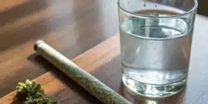 Realistic image showing a cannabis joint next to a glass of water, symbolizing the connection between pot use and dry mouth.