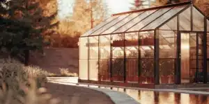 Hyper-realistic scene of a glass greenhouse at sunset, with golden light reflecting in a water feature.