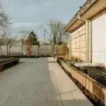 Organized backyard garden with potted flowers and vegetables along a house wall.