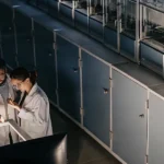 Two researchers in lab coats examining cannabis biotech equipment under lab lighting.