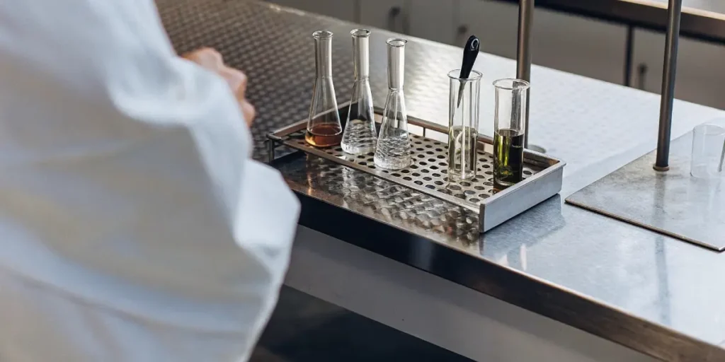 Various cannabis extraction containers with different liquids in a metal rack on a lab bench.