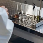 Various cannabis extraction containers with different liquids in a metal rack on a lab bench.