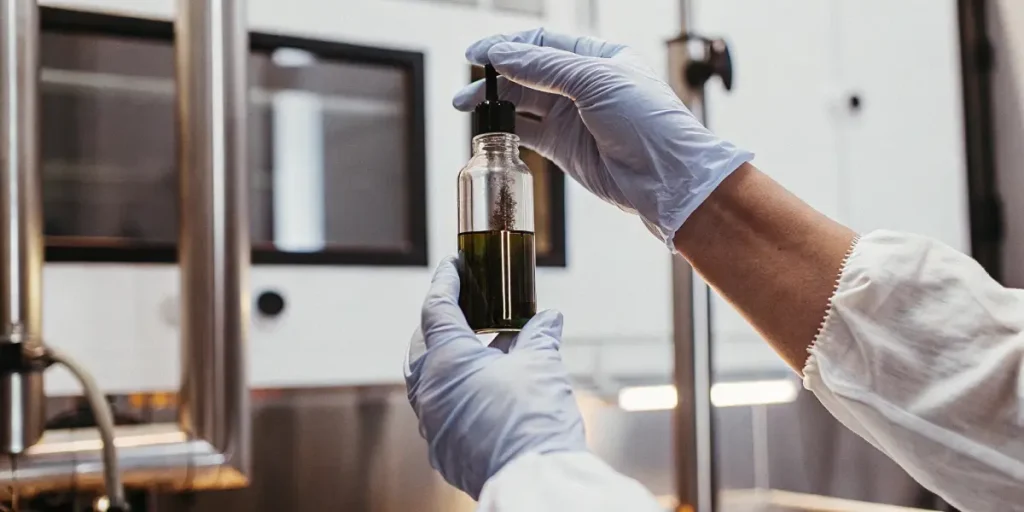 close-up of a scientist's gloved hands holding a glass dropper bottle filled with cannabis oil