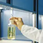 Scientist in white coat examining a cannabis leaf in oil inside a lab bottle