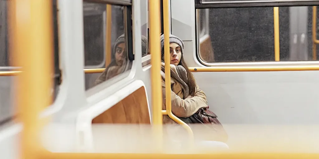 Young woman in a beanie sitting alone on a city bus at night, looking reflective.