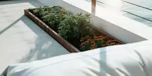 Raised garden bed with cannabis plants and orange flowers on a sunny patio.