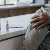 Close-up of an elderly person touching their aching knee with CBD drops and medication placed on a counter.
